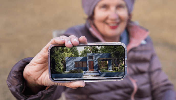 A Los Angeles resident holding a smartphone showing a planned rebuilt home