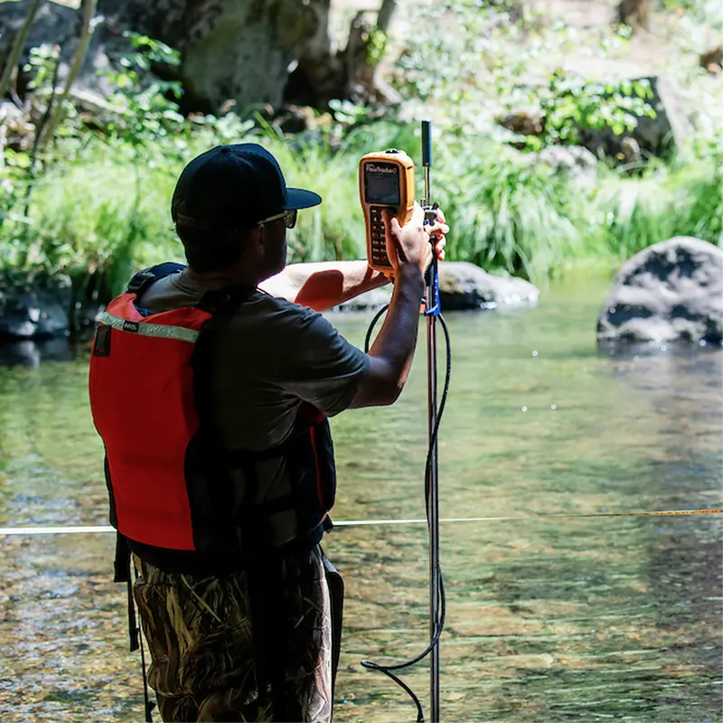A technician standing in a river measuring with an instrument