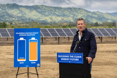 Governor Newsom speaking at a podium reading "Building the clean energy future" in front of solar panels