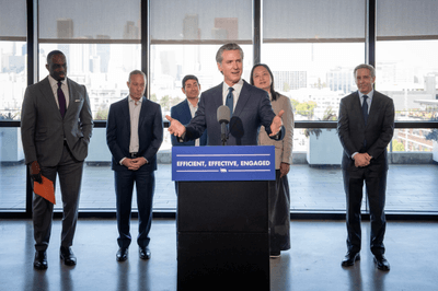 Governor Newsom speaking at a podium with a sign reading "Efficient, effective, engaged"