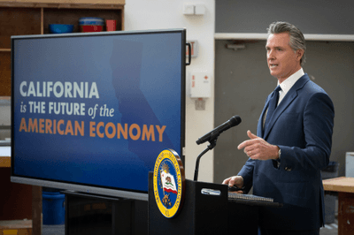 Governor Newsom speaking at a podium next to a screen reading "California is the future of the American economy"