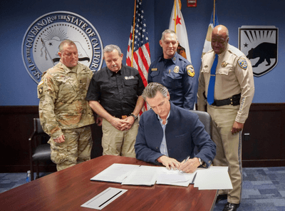 Governor Newsom signing executive order with emergency response officials standing behind him